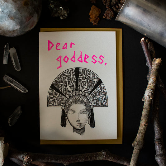 A deity with a half circle head dress with the text "Dear Goddess" above it and gold envelope behind it.
