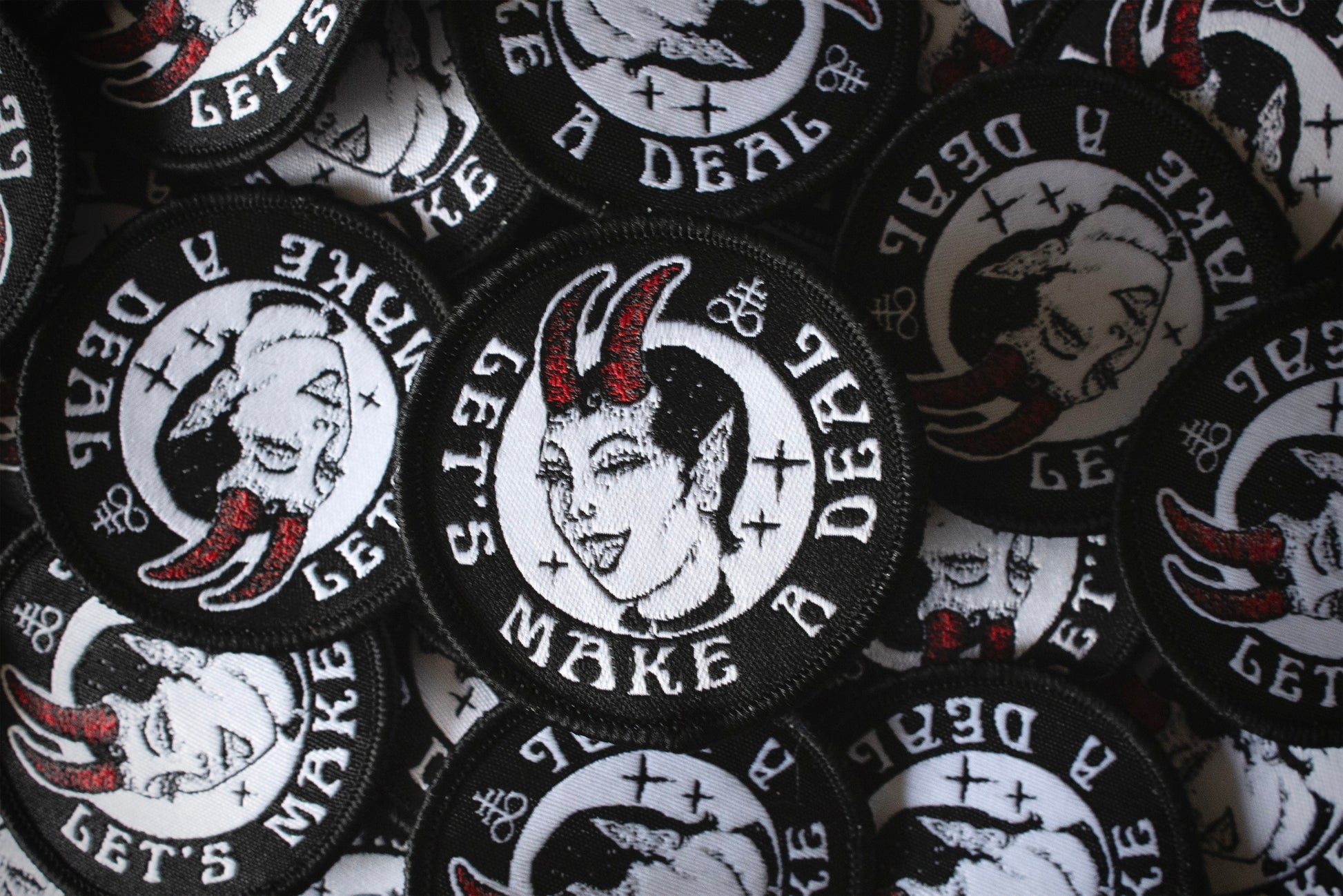 A round patch with the text let's make a deal, a devil woman winking, featuring a leviathan cross