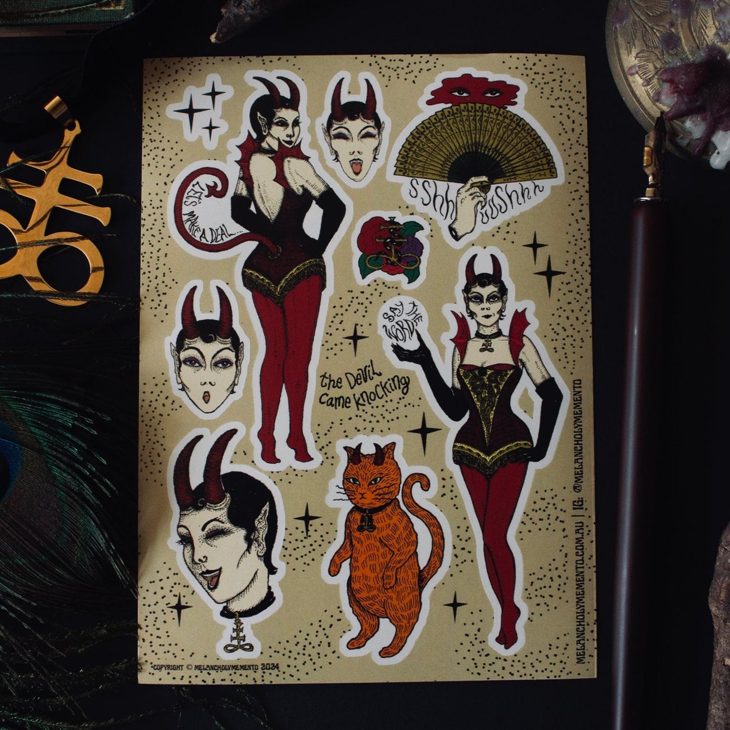 Devil Came Knocking sticker sheet surrounded by peacock feathers, leviathan cross, and a calligraphy pen.