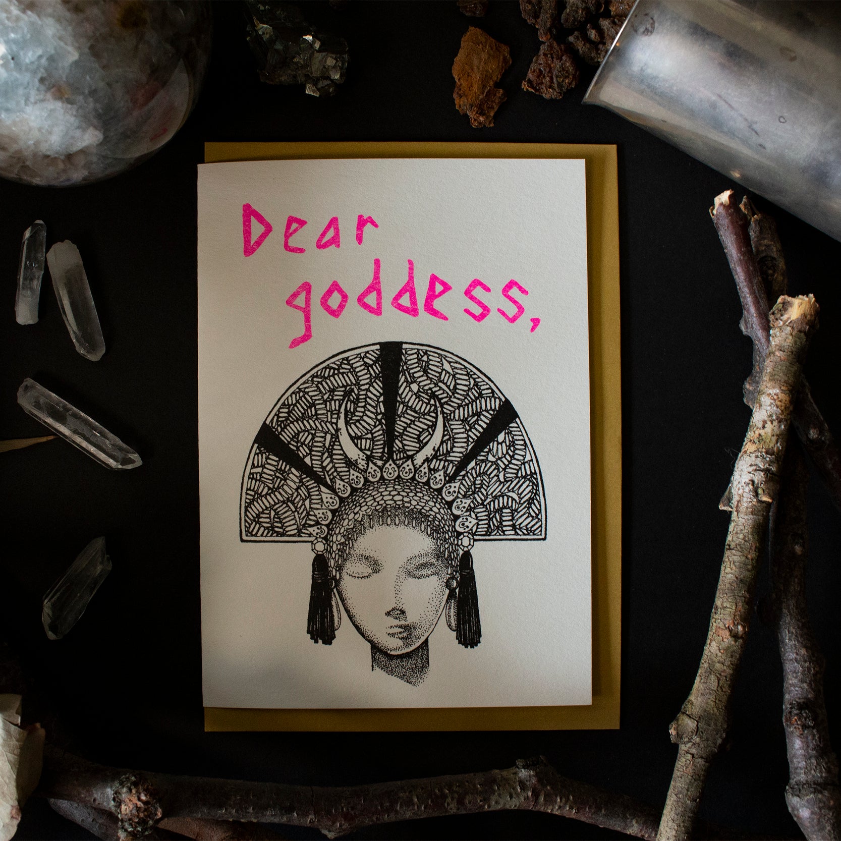 A deity with a half circle head dress with the text "Dear Goddess" above it and gold envelope behind it. 
